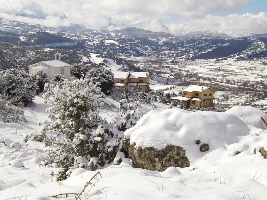 Τα σπίτια και η πλαγιά χιονισμένα, με τα βουνά στο βάθος